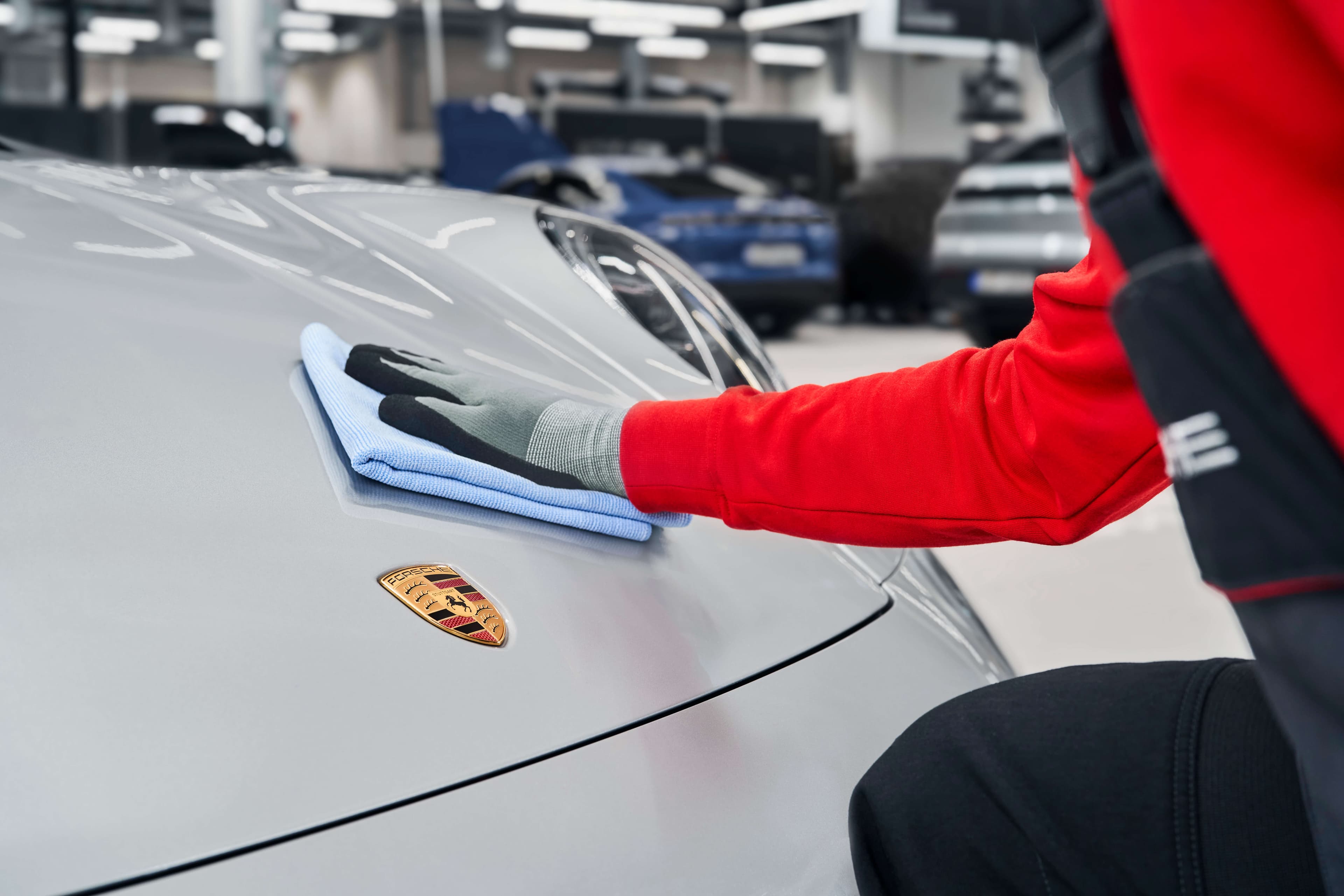 Porsche Technician polishing a silver Porsche car hood with a blue cloth in a Porsche Service Center.